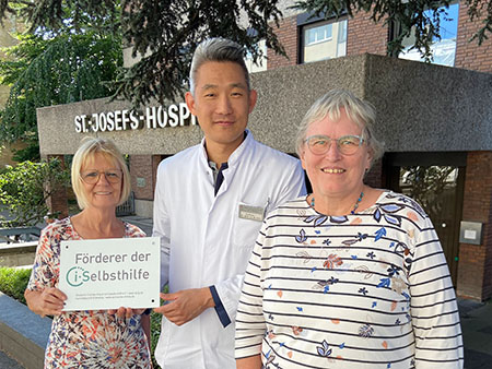 Sonja Ohligmacher, Marion Hölterhoff überreichen Prof. Park die Plakette mit Logo